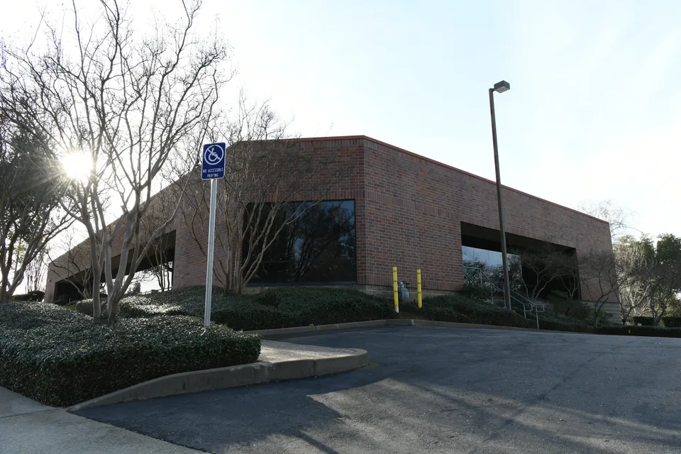 Illustrative photograph: Low brick office building with dark glazing, planted borders and a paved approach